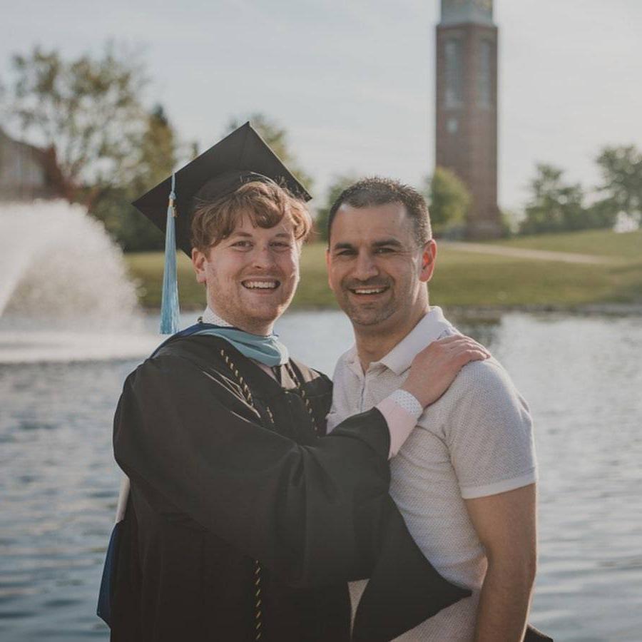 Luke Madden embracing someone while wearing his cap and gown, with the Cook Carillon clocktower in the background